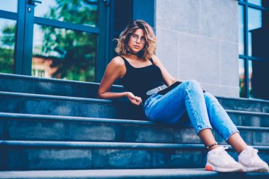 Merdivenlerde serbest zaman açık havada sırasında oturan muhteşem kız gözlük ve ödeme merdivenlerde yalan kamera bakarak modern giyimleri şık Eyewear ciddi kadın hipster portresi