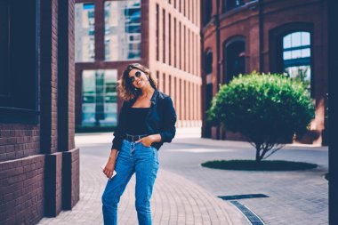 Kentsel ayarı arka planda, Bahar hafta sonları caddenin üzerinde yürüyen güneş gözlüğü mutlu hippi kız poz trendy casual göz varoluş portre çekici beyaz modeli giymiş