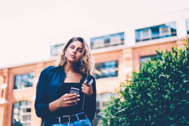 Ciddi kadın şık giyim bildirim kamera ayakta tanıtım alanı, cep telefonu üzerinden sosyal ağlar sohbet çekici hippi kız portresi yakınında bakarak akıllı kontrol