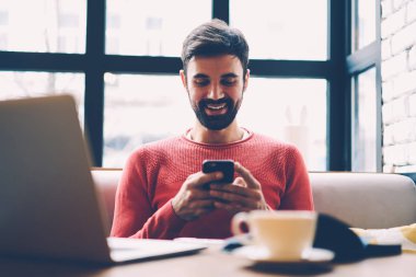 Smartphone sahip break kahve dükkanında arkadaş sohbet üzerinde geri göndermeye sakallı hippi adam gülümsüyor, vasıflı serbest meslek almak iyi iş teklifi online proje dizüstü bilgisayar kullanarak yapmak için