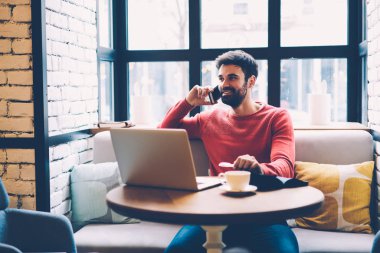 Pozitif hipster adam Smartphone'da uzaktan, çalışma dizüstü bilgisayarda yazılım yükleme sırasında hafta sonu için plan tartışırken genç işadamı kafede mobil konuşmayı dinlenme bahsediyoruz