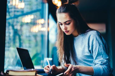 Genç yetenekli grafik tasarımcı bilgileri masada oturan Defteri'ne yazma şık elbise giymiş. Sevimli kadın bağlı 4 g Smartphone uygulama kullanarak zamanlaması planlama durulması