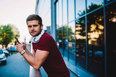 Online sosyal ağlar açık havada duran gökdelen arkadaşlarıyla sohbet ederken kameraya gülümseyen boynundaki modern kulaklık şık yakışıklı adamla yarım uzunluk portre. Kopyalama alanı alanı