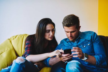 Şık coworking uzayda oturan smartphone yeni mobil uygulama yükleme hipster çocuklar. Internet üzerinde yeni gönderi yayımlama rahat kıyafet şık erkek ve kadın giyinmiş