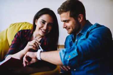 Gündelik kıyafeti kameraya smartwatch şık coworking yer poufs üstünde oturan erkek arkadaşı ile birlikte zamanında eğitim sırasında yüzünde gülümseme ile seyir güzel hippi kız portresi