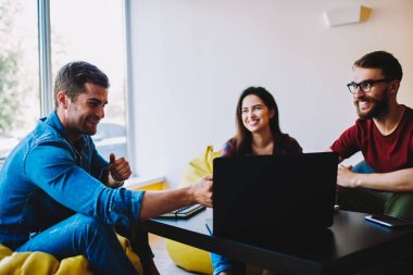 Erkek ve dişi BT uzmanları çalışmaları sırasında gülüyor break üzerinde rahat poufs oturan. Uzay coworking, dizüstü bilgisayar, oturmak komik konuşma sırasında eğlenmek pozitif arkadaşlar