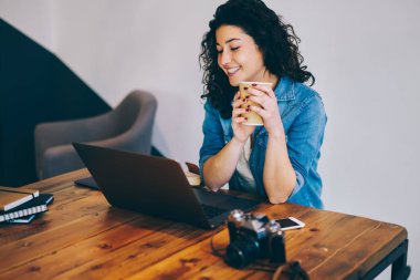 Genç gülümseyen hippi kız casual giyim Web sitesinde dizüstü bilgisayar izlerken ilginç video wifi için bağlı giymiş. Kapalı çalışırken içecek zevk neşeli kadın serbest meslek