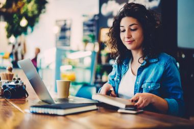 Güzel yaratıcı grafik tasarımcı ahşap masada oturan ve online ders başlatmak için hazırlanıyor gündelik kıyafeti giymiş. Not defteri ve aygıt kullanarak kahve dükkanında çalışan büyüleyici kadın kişi