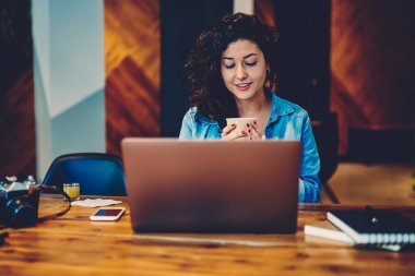 Popüler web sitesinde video izlerken ve aroma içeceğinizi kıvırcık saçlı hoş yaratıcı kadın yazarı. Çekici kadın kapalı dizüstü bilgisayarda uzaktan çalışma sırasında kahve molası