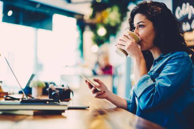 Uzaktan gadget kafede üzerinde çalışırken aroma kahveyi içiyor çekici akıllı grafik tasarımcı. İçecek servisi telefonla bankacılık yoluyla online para aktarma sırasında zevk genç kadın kişi