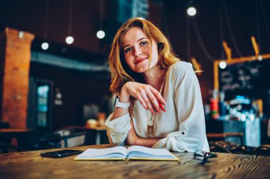 Başarılı işkadını sahip kırmak not defteri, günlük program hakkında kafeterya iç düşüncesinde gülümseyen güzel kadın Yöneticisi zevk dinlenme kameraya bakarak masada oturan portresi