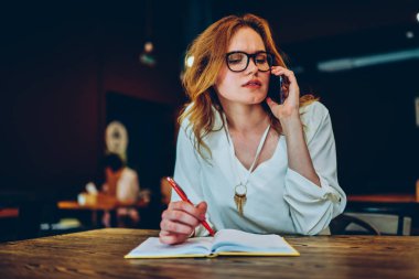 Dalgın işkadını sorun meslektaşı ile telefonda konuşurken ve notlar, düşünceli erkek mobil sohbet Cafe iç oturan Not Defteri'nde yazma bilgi analiz yapma çözme