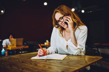 Başarılı kadın girişimci başlangıç mobil konuşma, Not Defteri'nde kişinin yazma meslektaşı ile telefonda konuşurken iş mutlu genç sahibi sırasında notlar yapmak için yaratıcı bir fikir tartışıyor