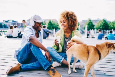 Neşeli afro Amerikan erkek ve dişi hipster şaka ve sahip eğlenceli oturan kare, sevimli köpek, Birbirinizle konuşmak güneşli bahar günü Tarih sırasında ilk tarihi gülüyor aşık Romantik Çift