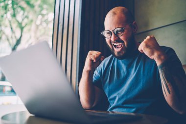 Kutluyor ve dizüstü bilgisayar üzerinden favori takım ile canlı yayın izlerken el hareketi serin Eyewear sakallı olumlu erkek kişi. Mutlu adam duygusal başarılı web sitesi yayında tepki