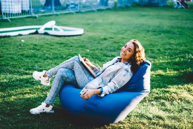 Yarım uzunluk portre neşeli genç kadının üzerinde kabarık kentsel ortamda ders kitabı ile ise kameraya bakıyor ve gülümsüyor. Pozitif hippi kız parkta zaman eğlence zevk