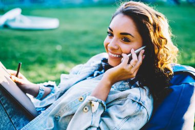 Telefon ile arkadaş Park toplantı söz güzel kahverengi gözleri ile neşeli kadın Tasarımcısı. Pozitif öğrenci yeni sturtup projenin serin düşünce hücresel zevk ücretsiz zamanında tartışıyor