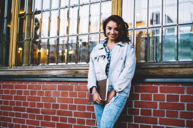 Casual denim konfeksiyon ders kitabı el Üniversitesi yapı tanıtım arka plan üzerinde duran ve kamera kopyalama alanı alanı yakınındaki gülümseyen holding neşeli güzel öğrenci portresi giymiş