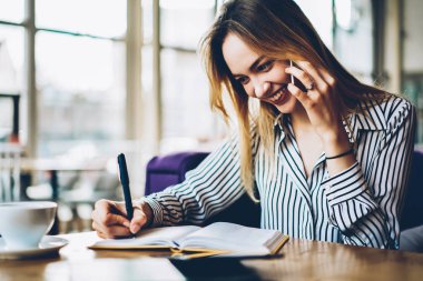 Pozitif sarışın Tasarımcısı not defteri bilgileri yazarken telefon görüşme sırasında arkadaşıyla konuşuyor. Telefon yoluyla iletişim ve metnin yanında kopyalama alanı alanı belirterek neşeli öğrenci