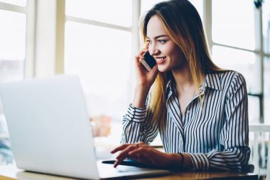 Dizüstü bilgisayar üzerinde rezervasyon denetlerken Smartphone'da müşteri ile konuşurken mutlu genç profesyonel Yöneticisi. Pozitif öğrenci ile arkadaş kopyalama alanı alanı yakınındaki Kurs hakkında mobil iletişim