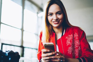 Çekici genç kadın blogger takipçileri ile sohbet ve Multimedya paylaşımı kamera Cafe iç reklam için reklam alanı yakınında oturan bakarken gülümseyen, yarı uzunluk portre