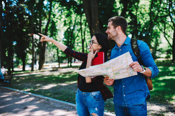 Female passerby with literature book pointing on right rout to experienced male traveller.Cheerful tourist with map in hands looking at direction that attractive student shows standing outdoors