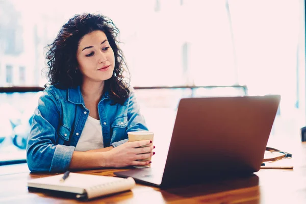 Skilled female graphic designer watching useful training webinar in website on laptop computer connected to wireless internet.Charming student enjoying interesting movie during break in coffee shop