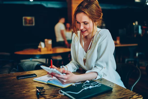 微笑的女实业家在网上使用便携式 进行研究在咖啡馆内部的远程工作 积极的女性阅读新闻和使笔记满意的生产工作在咖啡馆与 Wifi — 图库照片