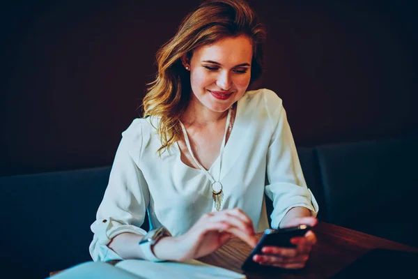 Smiling female happy getting message from friend texting feedback during work break in cafe,cheerful cute woman satisfied with installing new application on modern smartphone using internet connection