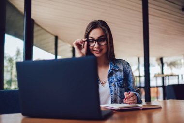 Çekici gülümseyen hippi kız moda gözlük kablosuz internet bağlantısı ile modern bilgisayar öğrenim. Sevimli öğrenci eğitim semineri izlerken sırasında aşağı not defterinde metin yazma