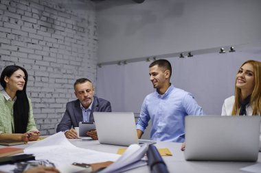 Deneyimli genç yaratıcı çalışanları ile birlikte çalışma sorunlarını çözme ve masada oturan dizüstü cihazlar ile proje geliştirme elinde dokunmatik yüzey ile mimari şirket müdürü 