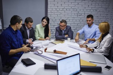 Beyin fırtınası sırasında yeni iş projesinin verimli çözüm üzerinde erkek ve kadın uzmanları teamworking. Deneyimli mimar toplantı masada oturan skeçler yapı üzerinde işbirliği yapma