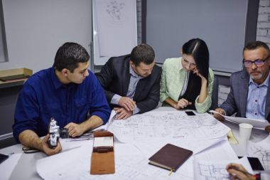 Profesyonel ekibi, deneyimli mühendis ofis iç tabloda toplantıda planlama oturma binanın mimari çizimler üzerinde çalışıyor. erkek ve kadın tasarımcılar planları üzerinde beyin fırtınası sırasında işbirliği