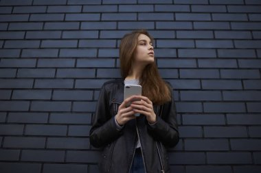 Hippi kız açık havada rahat kıyafet giymiş vakit arkadaşlarınızla sohbet sevimli siyah tuğla duvar promosyon arka plan, smartphone ile ayakta çekici kız öğrenci konsantre