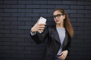 Profil resmi sosyal ağlar, çekici genç kız fotoğraf ayakta promosyon arka plan üzerinde yapma güncelleştirme smartphone kamera selfie yapma düşünceli genç kız öğrencinin portresi