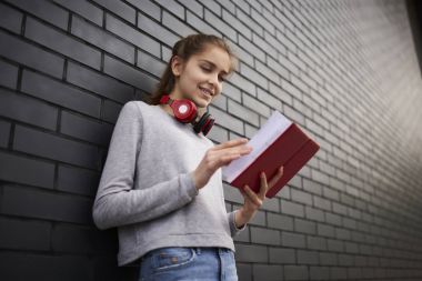 Gülümseyen genç kız, reklam mesajları için kopyalama alanı alanı duran arkadaşlar için beklerken kitap okuma rahat trendy sweatshirt içinde kadın hipster zevk edebiyat açık havada giyinmiş