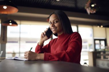 Gülümseyen afro Amerikan girişimci danışmanlık meslektaşı ile mobil seyredebileceğiniz fikir edinmek için çekici koyu tenli öğrenci caf ödev yaparken arkadaşıyla telefonda konuşurken sahip portresi