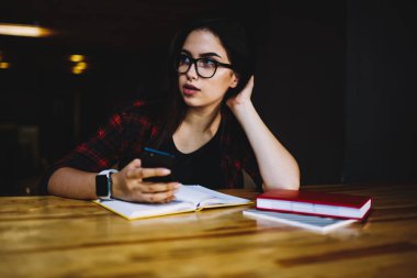 Uzağa bakarak ve telefon kullanarak takipçileri ile sohbet ederken kişisel web sitesi içerik için iyi fikirler düşünmeye yaratıcı esmer blogger durulması kapalı kablosuz internet'e bağlı