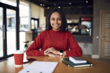 Esmer kadın İdari İşler Müdürü coffee shop işgal, neşeli afro Amerikan girişimci defter ve belgeleri jo için hazır ile işyerinde oturan memnun portresi