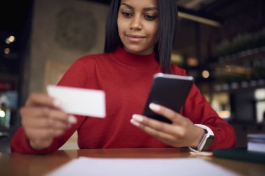 Kendine güvenen afro Amerikan işkadını kişi bankacılık hizmet ve çek hesabı, yatırımcı sayısı boş kartı çevirme smartphone üzerinde tutarak esmer İdari İşler Müdürü ziyaret kart kullanarak