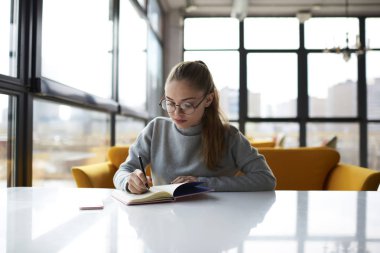 Dalgın kız öğrencinin not defterinde kompozisyon yazma modern iç kafede ödev. Gözlük numaraları ve hesaplama için mali dosya belirterek içinde profesyonel İdari İşler Müdürü