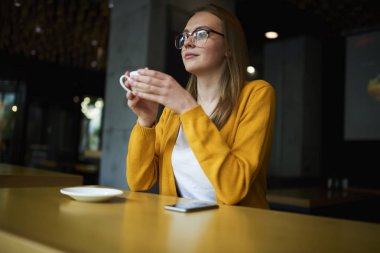 Lezzetli kahve elinde tutan ve uzağa bakarak şık gözlük düşünceli bir genç kadın. Düşünceli hippi kız planları hakkında düşünme ve sıcak içecek keyfi optik gözlük