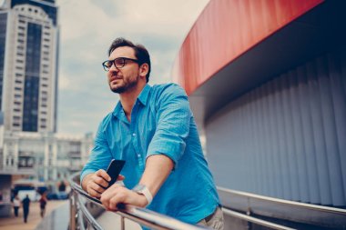 Dalgın sakallı hippi adam açık havada modern kentsel ayarı arka plan, cityscape yeniden oluşturmayı seyir gözlük yakışıklı erkek Gezgin üzerinde duran boş vaktinizi trendy kıyafetler giymiş