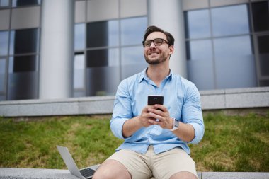 Gülümseyen yakışıklı öğrenci sosyal ağlar açık havada, 4 g bağlantı üzerinde mobil fotoğraf ve video gönderme Üniversitesi kampus içinde zevk hipster adam yeniden arkadaşımdan komik video alma gülüyor