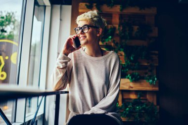 Kafe iç dinlenme ve arkadaş ile hareket eden, neşeli genç kadın eğlence sırasında telefonla iletişim şık kısa saç modeli ile görüşmekte gözlük mutlu şık giyimli hippi kız