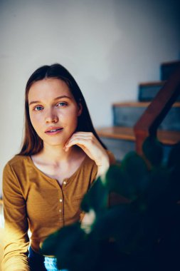 Kamera, doğal güzel genç kız öğrenci Kitaplığı'nda serbest zaman harcama bir şey üzerinde durulması bakarak kapalı bitki yakınındaki merdivenlerde oturan dalgın genç kadın portresi yarım uzunluk