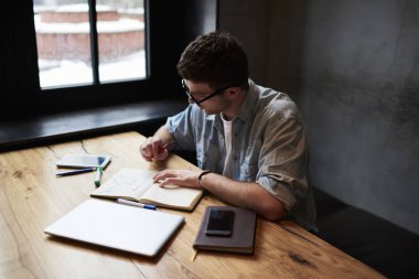 Üstten Görünüm yetenekli erkek Tasarımcısı defter vasıl okul sırası studio iç modern araçlar ile oturan yeni grafik çizimler çizim kot gömlek giymiş. Projede çalışan dalgın mimar