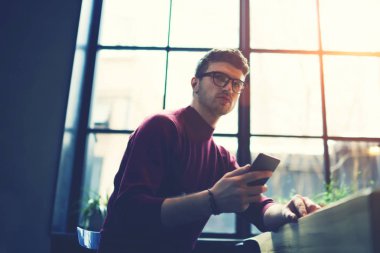 Optik Gözlük tarafında yer coworking oturan bakarken modern telefon elinde tutan ciddi erkek öğrencinin alt görünümü. Gözlük ile dijital smartphone dalgın girişimci 