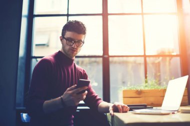 Dalgın hipster adam gözlük sınavlarına hazırlamak için arkadaş telefonu Üniversitesi'nde oturan ve dizüstü bilgisayar cihaz eğitim Ücretsiz 4 g internet bağlantısı üzerinden sms mesajı gönderme