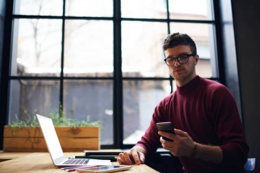 Dalgın hipster adam gözlük sınavlarına hazırlamak için arkadaş telefonu Üniversitesi'nde oturan ve dizüstü bilgisayar cihaz eğitim Ücretsiz 4 g internet bağlantısı üzerinden sms mesajı gönderme